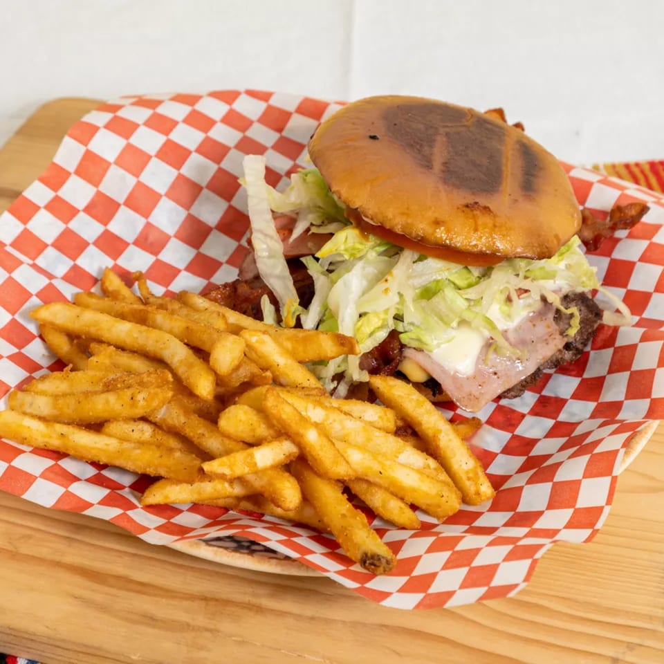 A burger with lettuce, tomato, bacon, and cheese, served with a side of seasoned fries.